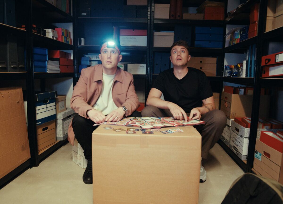 Roman Kemp and Chris Stark sit together in a dark store room, going through their Topps sticker collection.