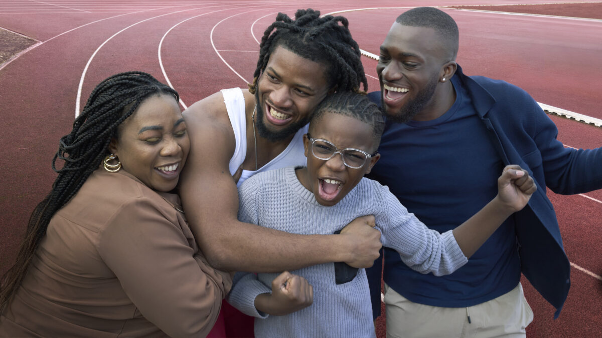 Emmanuel Oyinbo-Cocker surrounded by his family on the running track. They are all smiling and embracing one another, showing how key support is to Oyinbo-Cocker's work on the track.