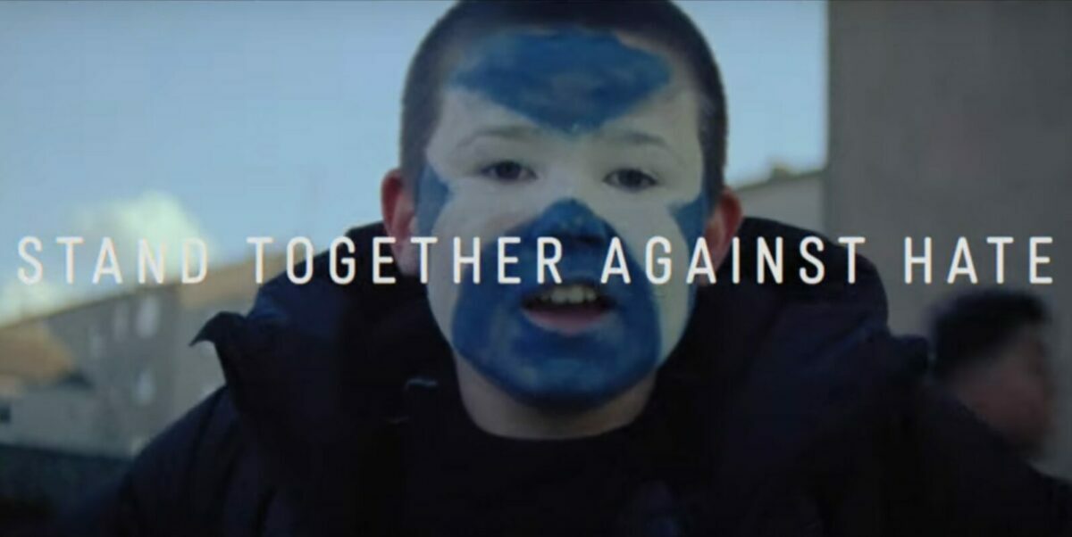 A passionate Scotland fand has St Andrew's flag painted across his face. Text in front reads "Stand together Against Hate".
